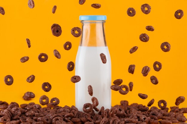 Yellow milk bottle on yellow. Chocolate cereals rings falling around.