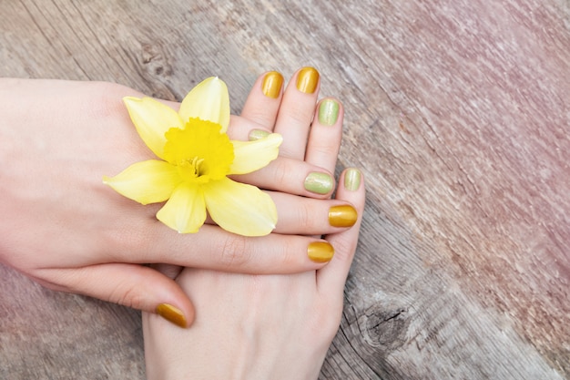 黄色のネイルデザイン。水仙の花を保持しているキラキラのマニキュアで女性の手。