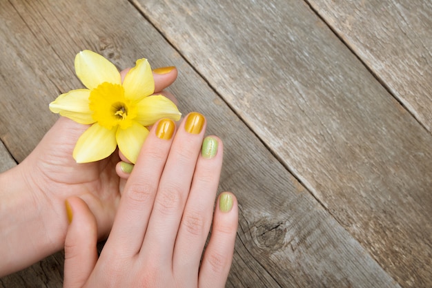 Yellow nail design. Female hand with glitter manicure holding narcissus flowers.