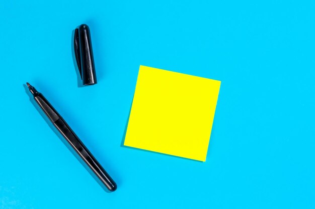 Yellow note with empty place for text with marker on blue background flat lay