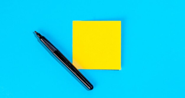 Yellow note with empty place for text with marker on blue background flat lay