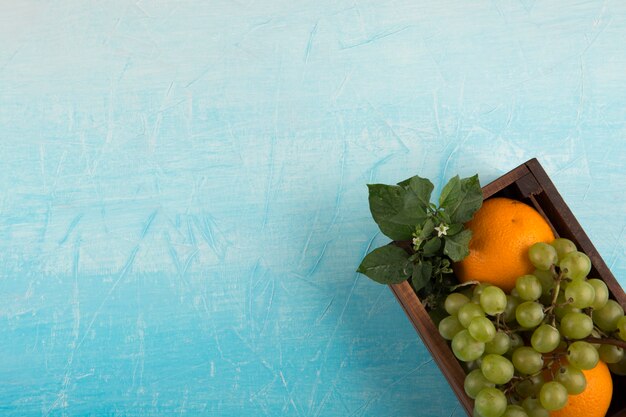 Yellow oranges and a bunch of grape in a wooden box in the corner