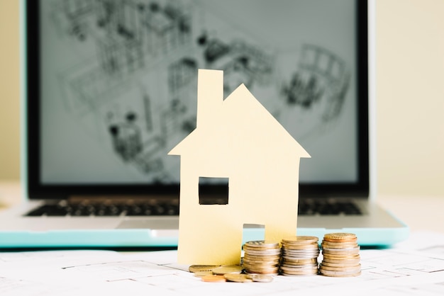 Yellow paper house and coins at laptop