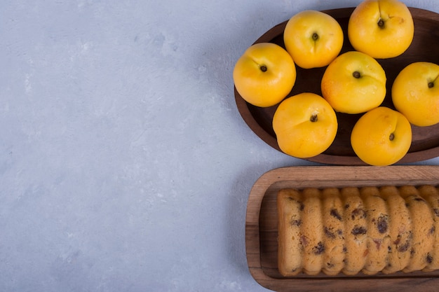 Yellow peaches and rollcake in wooden platters on blue space
