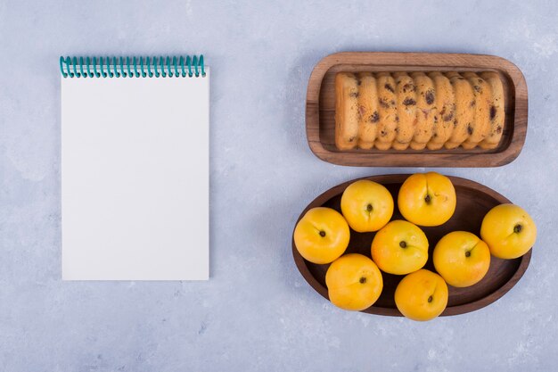 Yellow peaches and rollcake in wooden platters with a notebook aside
