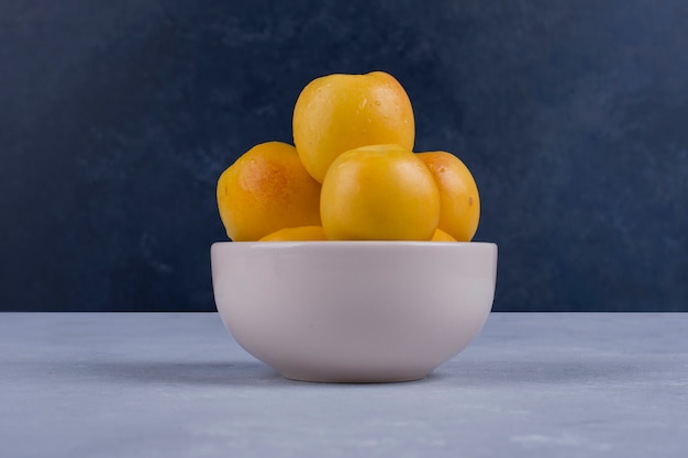 Yellow peaches in a white ceramic bowl isolated on blue