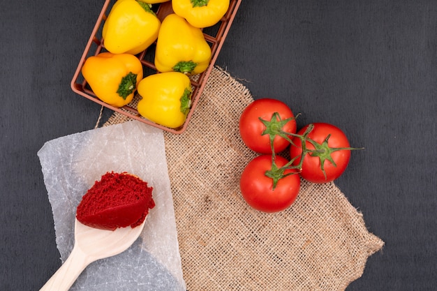 Merce nel carrello gialla del pepe vicino ad un mazzo di pomodori e di passata di pomodoro in cucchiaio sul nero