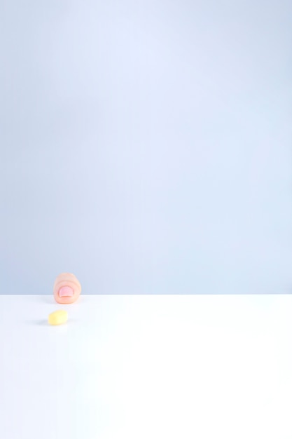 Yellow pill in front of human finger on white table