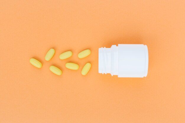 Download Free Photo Yellow Pills Spilled From White Plastic Bottle On An Orange Background PSD Mockup Templates