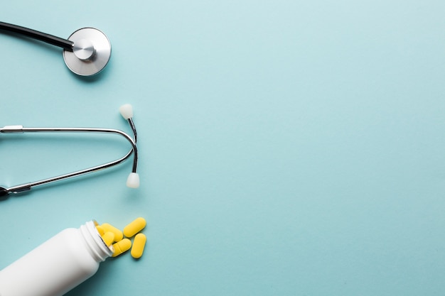 Yellow pills spilling out from white bottle near stethoscope over blue surface