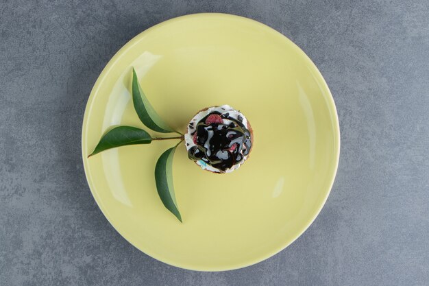 An yellow plate with delicious creamy cupcake on a gray surface