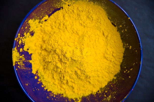 Free photo yellow powder inside the blue bowl against black background