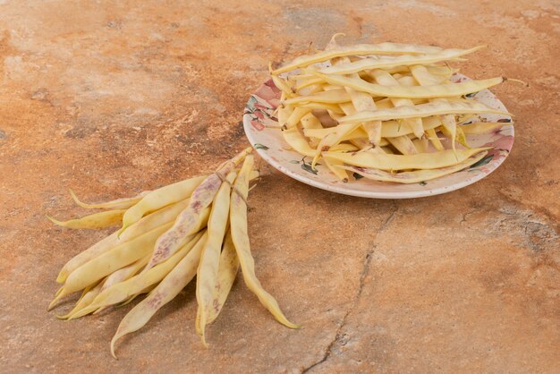 Yellow raw beans on plate and on orange surface.