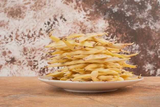 Yellow raw beans on plate and on orange surface.