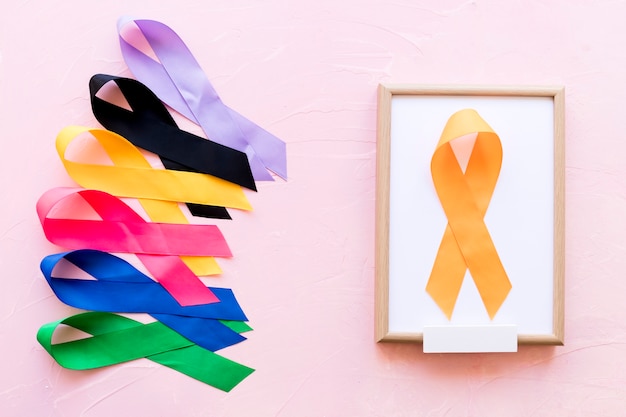 Free photo yellow ribbon on white wooden frame near the row of colorful awareness ribbon