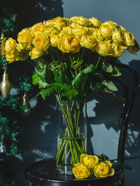 Желтые розы внутри прозрачной стеклянной вазы с водой на стуле.