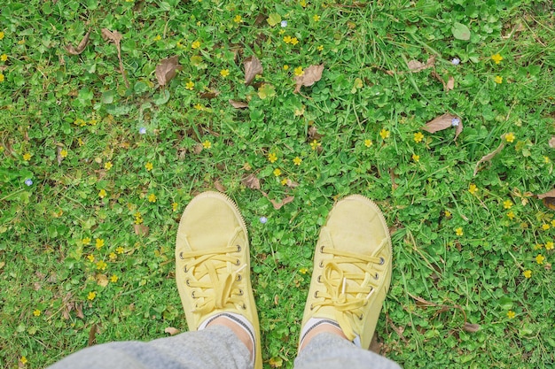 Yellow sneakers on a green spring meadow with yellow flowers the beginning of spring and travel time first person point of view top view with copy space idea for background or postcard