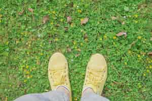 Free photo yellow sneakers on a green spring meadow with yellow flowers the beginning of spring and travel time first person point of view top view with copy space idea for background or postcard