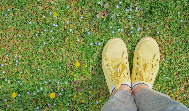 Free photo yellow sneakers on a green spring meadow with yellow flowers the beginning of spring and travel time first person point of view top view with copy space idea for background or postcard