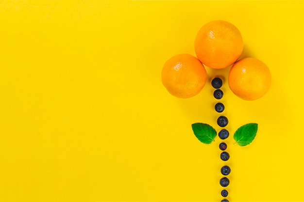 Yellow surface with flower made of summer fruits