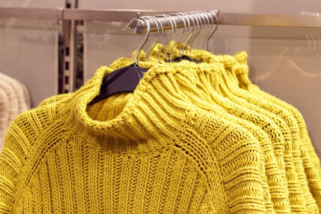 Желтые свитера, висящие на вешалках в магазине, концепция покупки одежды