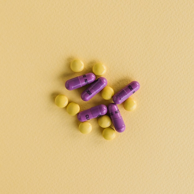 Желтые таблетки и фиолетовые капсулы на текстурированном фоне