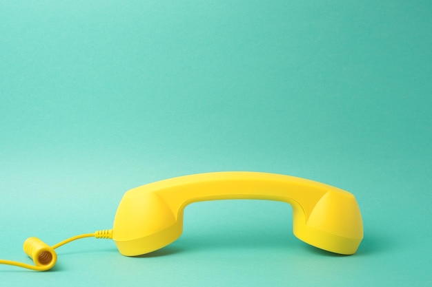 Free photo yellow telephone receiver on turquoise background