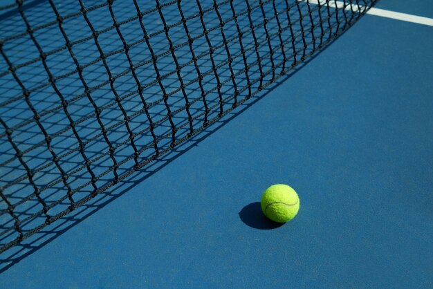 노란색 테니스 공은 검은 테니스 코트의 그물 근처에 누워 있습니다.