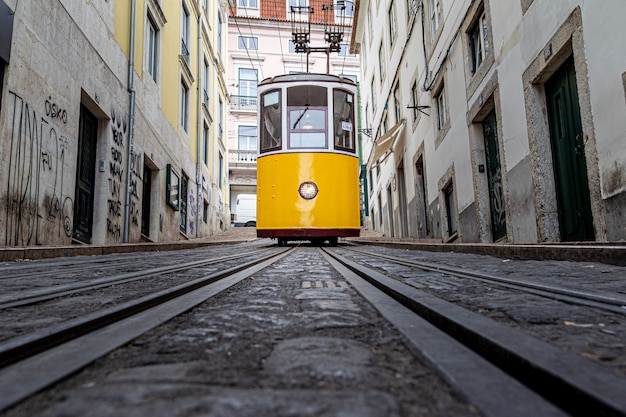 Желтый трамвай идет по узкой аллее в окружении старых зданий