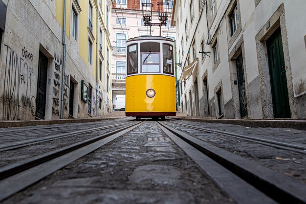 Yellow tram going down a narrow alley surrounded by old buildings