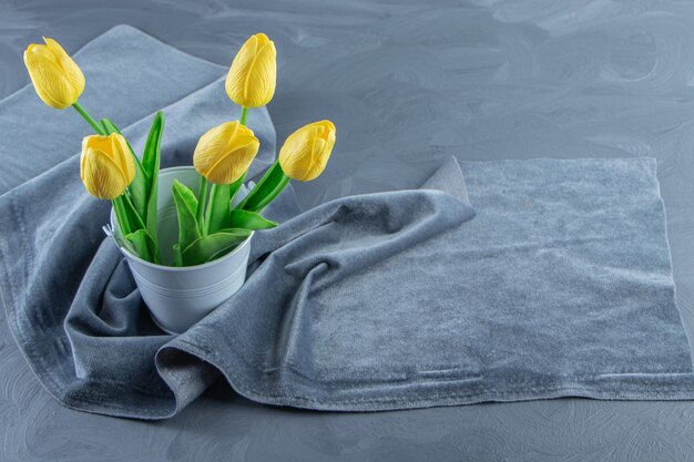 Желтые тюльпаны в ведре на куске ткани, на белом фоне. Фото высокого качества