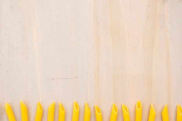 Желтые сырые макароны пенне расположены в ряд на деревянном фоне текстурированных