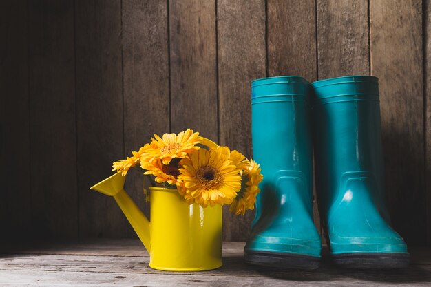 Yellow watering can with flowers next to plastic boots