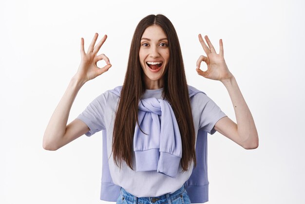 Yes agree Smiling happy woman showing okay OK gesture nod in approval like and approve support your choice praise nice work standing over white background