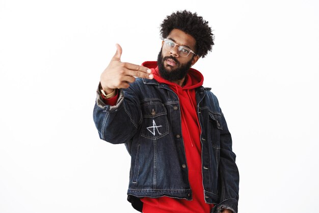 Yo my outfit lit. Portrait of cool and stylish self-satisfied confident man with beard and afro hairstyle reading rap making gun gesture as singing hip-hop tilting head posing on gray.