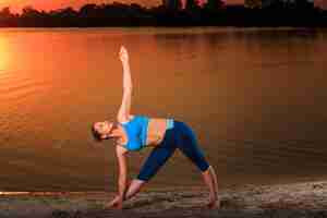 Free photo yoga at sunset on the beach. woman doing yoga, performing asanas and enjoying life on the river