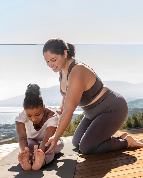 Yoga teacher helping woman with pose  full shot