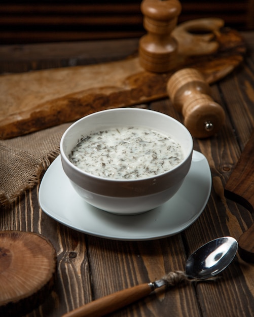 Yogurt soup with herbs inside white bowl.