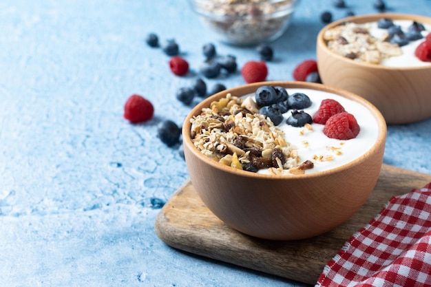 Yogurt con frutti di bosco e muesli per colazione in una ciotola su sfondo blu