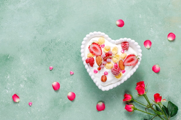 Yogurt with corn flakes and berries in a heart-shaped bowl.