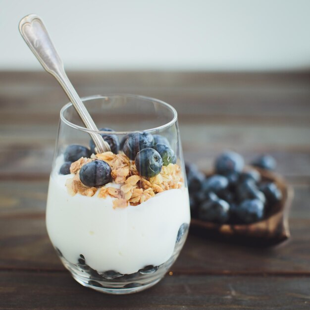Yogurt with granola and fresh blueberries in glass bowl over old wood background Vintage effect