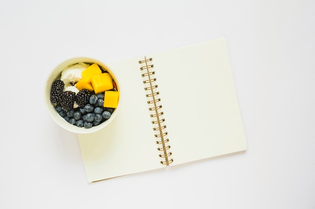 Yogurt with mango slices; blueberry and blackberry toppings in cup on spiral notebook
