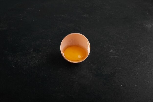 A yolk inside eggshell on black surface in the center. 