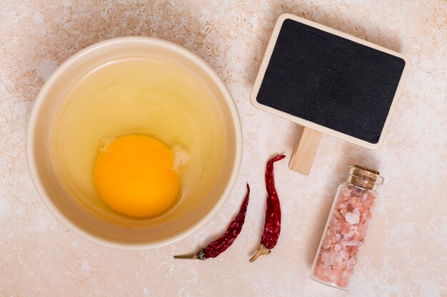 Желтки и яичный белок в миске с перцем чили; гималайская соль и пустой плакат