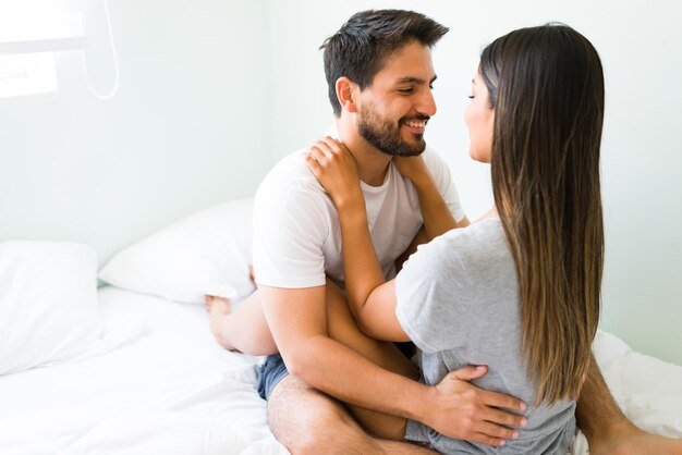 You are very beautiful. Handsome young man in comfy pajamas looking at her pretty girlfriend while hugging and cuddling in bed