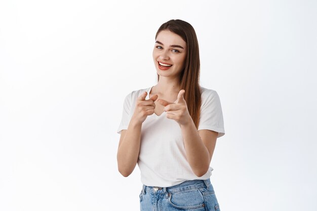 You got this, join us. Smiling assertive woman pointing at front, inviting to work for company, or to event, praising good job, well done gesture, standing over white wall