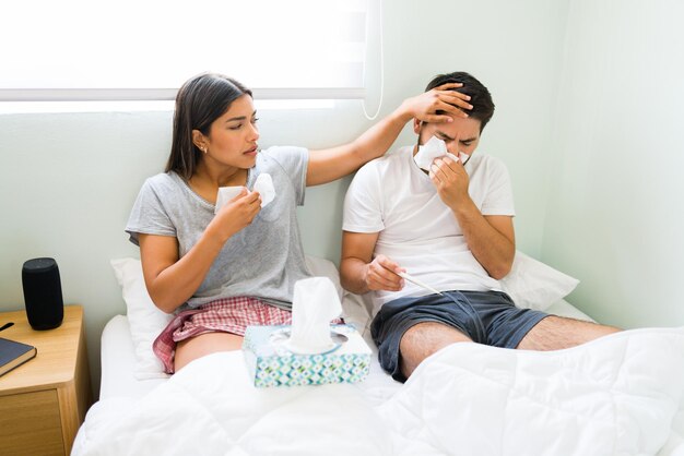 Do you have a fever? Loving girlfriend touching her boyfriend's forehead to feel his temperature while sick with a bad cold