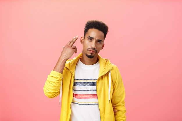 You kill my vibe. Gloomy irritated and annoyed handsome stylish african american guy in yellow trendy jacket showing finger gun gesture over temple as if shooting himself with bothered look