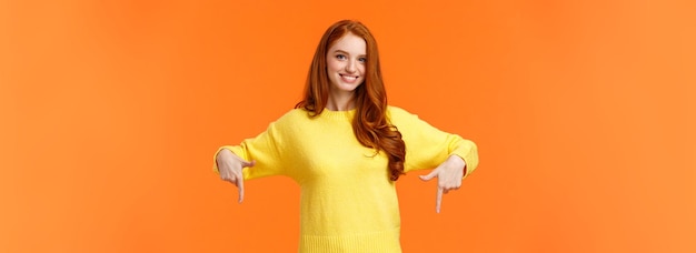 Free photo you need see this check it out cheerful gorgeous redhead girl in yellow sweater smiling and pointing