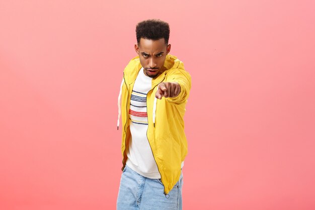 You will regret this. Portrait of threatening angry and pissed dangerous african american young man looking from under forehead with disdain and rage pointing at camera blaming someone over pink wall